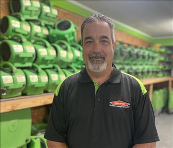 Male employee smiling in a black Servpro shirt with a green background