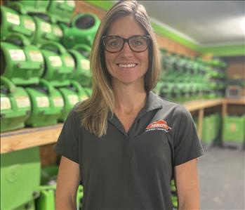 Brown haired employee in a black servpro shirt standing in front of a green background